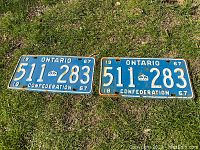 Both vintage 1967 Ontario license plates displayed on grass, showing front with blue paint and white embossed numbers '511-283' and text 'ONTARIO', 'CONFEDERATION'. Visible rust and wear on edges and mounting holes.