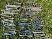 Multiple combination and adjustable wrenches laid out on grass showing full collection and varying sizes.