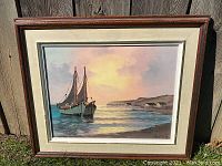 Frontal image of the framed original oil painting showing coastal scene with sailboats and houses in the background at sunset.