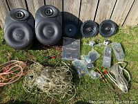Overview of lot showing 2 large Kaption audio speakers, 3 smaller speaker drivers, Kaption amplifier manual, audio cables, mounting brackets, and various connectors spread on grass surface.