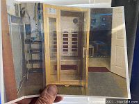 Printed photo of assembled sauna cabin showing glass door, wood slat panels and interior bench
