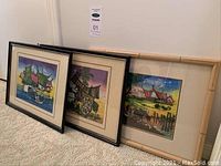 Three framed Asian-themed fabric pictures grouped on floor showing all three artworks and frames
