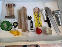 Drawer with wooden baking racks, metal grater, plastic and metal sifters, measuring spoons, wooden skewers, and miscellaneous small kitchen tools.