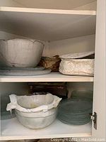 Shelves with stacked Aspen glass bowls and plates, including large bowls on top shelf and clear glass plates on lower shelf.