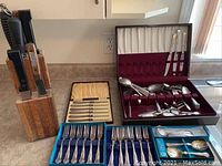 Overall view of silver plated flatware spread out on countertop with wooden knife block holding knives.