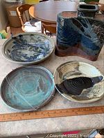 Three pottery plates and one jug displayed together on a table, showing size, shape, and glaze details.