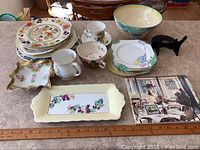 Shows assorted china items laid on counter including plates, bowls, cups, and placemats