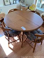 Full view of round maple table with four matching chairs and cushions around it, situated on wood floor near window.