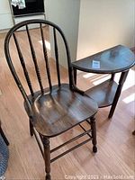 Photo showing both the vintage wooden chair with curved spindle back and the half-moon shaped side table with two shelves, wood finish worn with age.