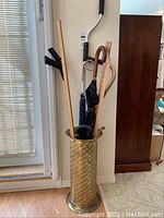 Overall view of brass umbrella stand holding multiple umbrellas and walking sticks. Shows arrangement and variety of items in the stand.
