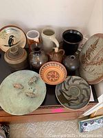 Assorted pottery plates, jugs, mugs, and vases displayed on a wooden surface.