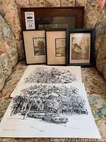 Group photo of sketches and framed artworks placed on a floral sofa. Shows various framed and unframed pieces, highlighting sizes and framing.