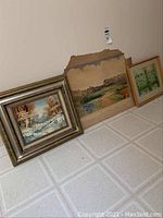 Photo of three vintage landscape paintings leaning against a wall, showing variety in size and frame style.
