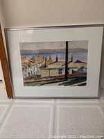 Framed watercolor painting showing coastal village with houses and distant water, prominent dark utility pole, measuring 9x13 inches