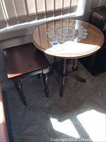 Side view showing the round glass-top side table with pedestal base and the small dark wood square side table.