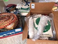 Box with assorted braided placemats, plastic-wrapped lace doilies and packaged French lace items
