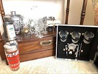 Overall lot showing wooden suitcase with barware items, glassware, ice buckets, red drink shaker, and metal accessories.