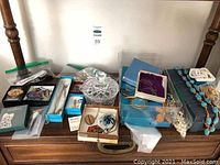 Overview of assorted costume jewelry and storage box on wooden dresser