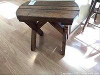 Side angle view of vintage wood bench on hardwood floor showing solid wood construction and angled legs.