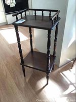 Full view of the vintage wooden side table showing turned legs, two shelves, and guard rails on the top shelf