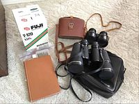 Lot overview showing all items: Fuji VHS tapes box, A.C. Lowe & Co opera glasses with leather case, Tasco binoculars with black case.