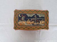 Top view of jewelry box showing painted scene of knight on horseback near a windmill under a moon and clouds, with decorative green and red borders.