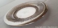 Side angle view showing the round nickelsilver Apollo Sheffield plate tray with pierced pattern and engraved center, showing signs of tarnish and needing cleaning.