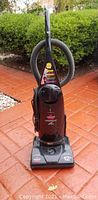 Front view of a dark red Bissell PowerForce upright vacuum cleaner with hoses and power cord on outdoor pavement.