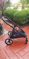 Black stroller frame outdoors with greenery in background.