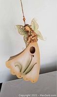 Front view showing the wooden birdhouse topped with a fairy figurine with green wings and a flared scalloped base with bird entrance hole.