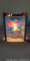Front view of the paper side table lamp showing illuminated image of Homer Simpson in green pants and blue shirt with colorful cloud background.