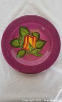 Top view of purple ceramic plate featuring a red and yellow pepper design with green leaves in center.
