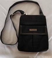 Front view of black cloth purse showing adjustable strap, front flap with metallic plaque, and compact size.