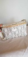 Front and side view of white Carolina Herrera purse showing gray CH logo print and beige zipper trim