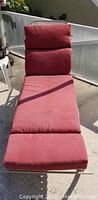 Photo of a single red polyester lounge chair cushion with segmented padding in three main sections for head, seat, and leg support on a concrete surface outside.