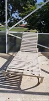 Photo of white plastic pool lounge chair placed outdoors on patio surface with a screened enclosure background.