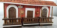 Front view of the detailed wooden Puerto Rican red house facade model showing doors, balconies, roof, and wall decorations.