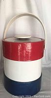 Front view of cylindrical plastic ice holder with blue bottom, white middle, and red top section, featuring a handle and lid.