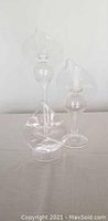 Three clear glass blown candlesticks with rounded, curved shapes standing on flat bases, shown from front view.