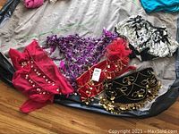 Full view of multiple belly dancer costume pieces laid out on a bed, showing various colorful hip scarves and belt pieces with coins and beads.