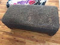 Full view of rectangular ottoman upholstered in paisley fabric with wood base and legs.