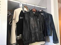 Three Hard Rock Café jackets hanging in a closet: black leather, cream/black baseball, and blue denim.