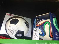 Photo showing autographed soccer ball in original Wilson packaging next to Brazooka box.