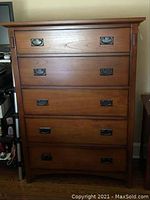 Front view of dresser with closed top and 5 drawers with black handles.