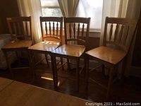 Four wooden dining chairs with high backs and vertical spindle design, set in front of windows.