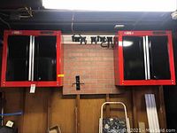 Two red and black Craftsman locking cabinets mounted side by side on a wood wall with mounting rail