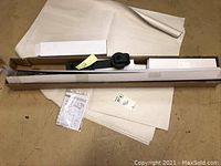 Photo of long metal barn door track rail in box packaging with instruction manual and mounting hardware lying on workshop floor.