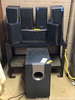 Full set of Onkyo speakers including subwoofer, center, surround, front, and back speakers arranged on a shelving unit.