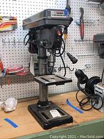Front and side view of the Central Machinery 12 speed bench drill press on a wooden workbench with tools in the background.