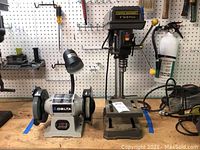 Both Central Machinery 8" drill press and Delta 6" bench grinder on wooden benchtop against pegboard wall